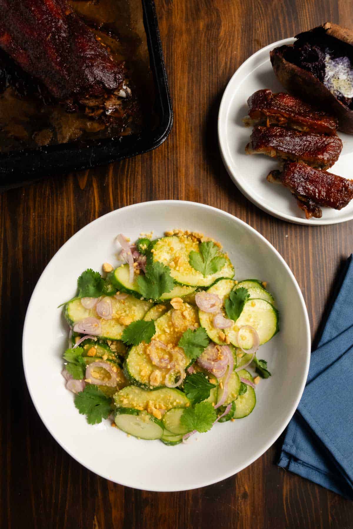 Spicy Thai cucumber salad with a tray of pork ribs with chipotle barbecue sauce and a baked purple sweet potato.