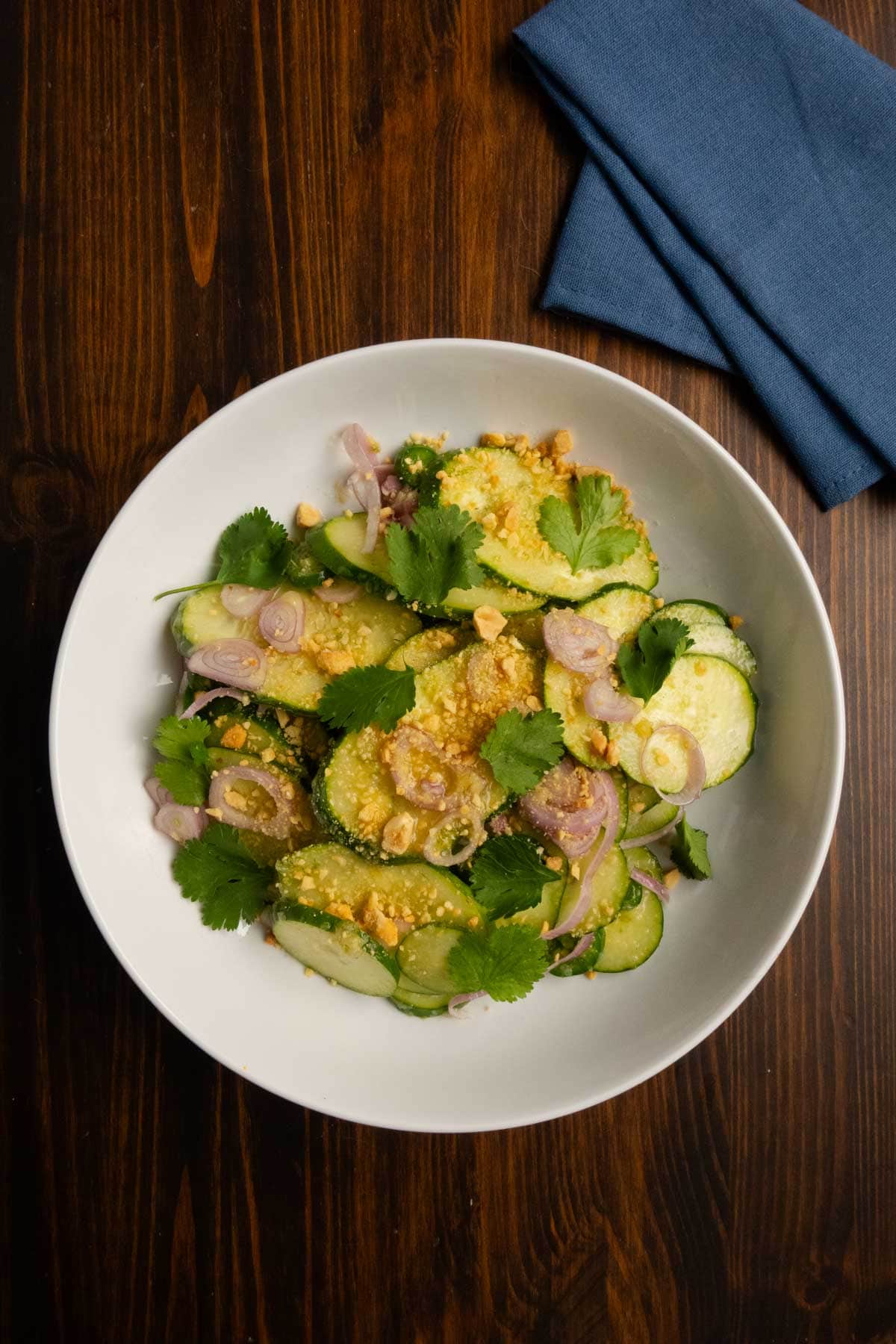 A bowl with spicy Thai cucumber salad in it with a blue napkin on the side.