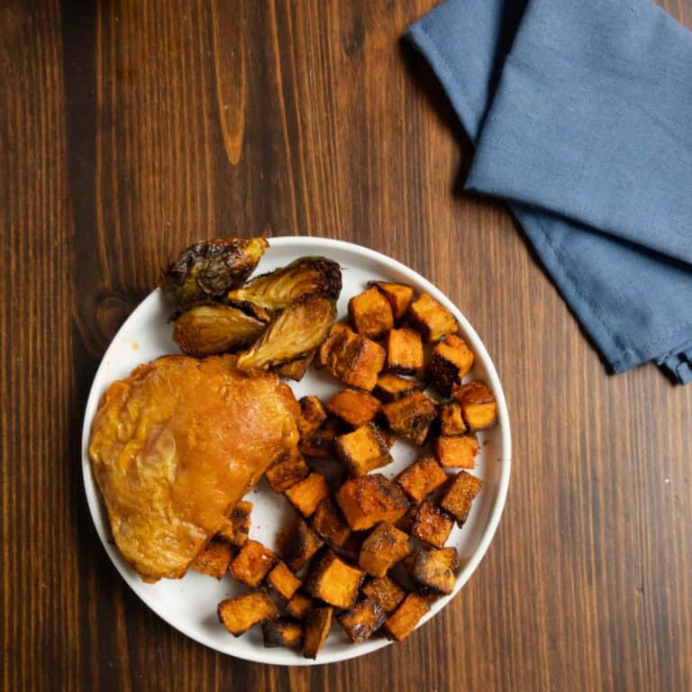 Crispy roasted sweet potato chunks on a plate with a dry brined chicken thigh.